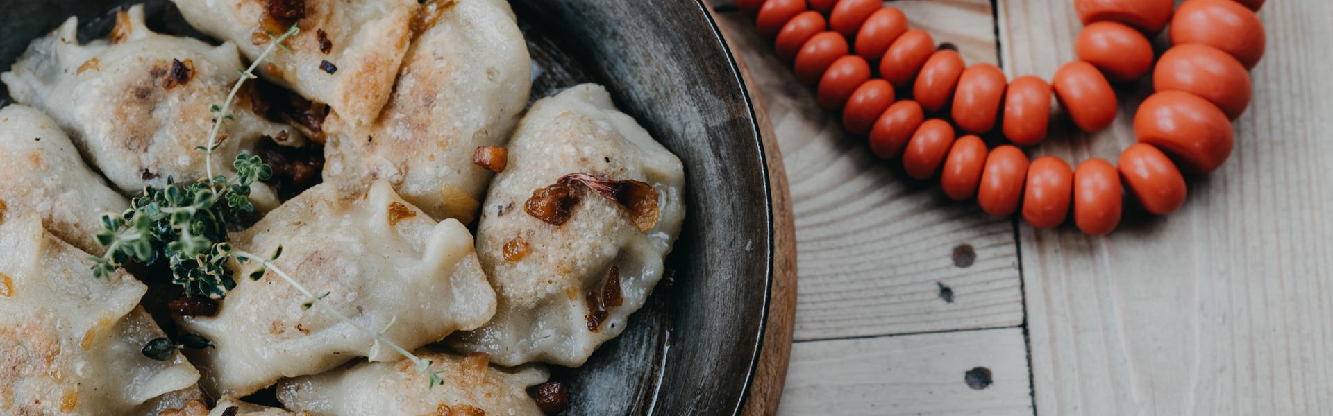 Ein Teller mit Pierogi, daneben eine Kette mit roten Perlen.