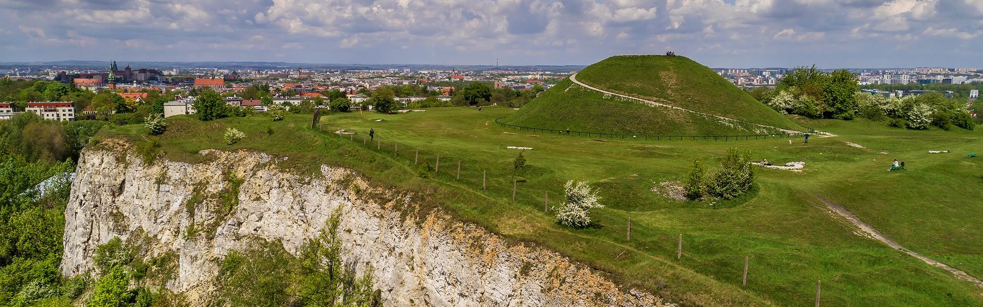 Duży, zielony kopiec ziemny, w tle widok na Kraków.