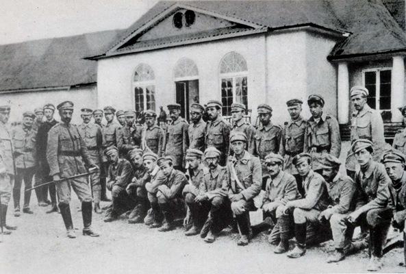 Siedzący przed murowanym budynkiem w stylu dworkowym żołnierze. Zdjęcie historyczne - czarno-białe.